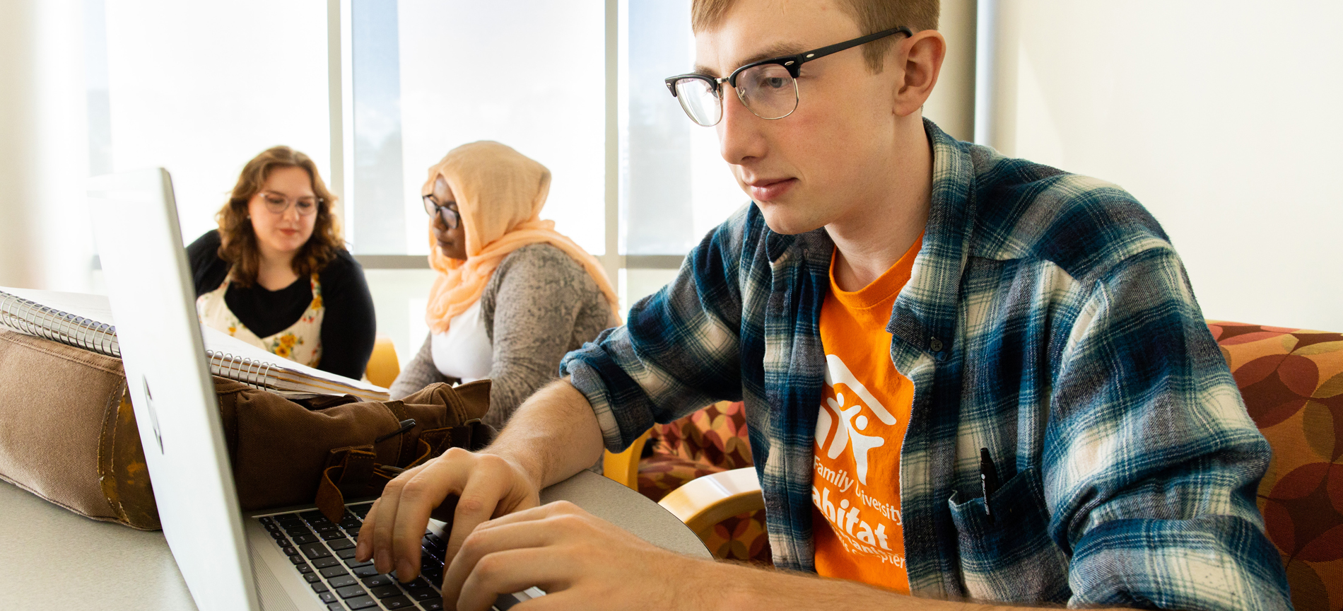 Guy on computer with 2 girls in background