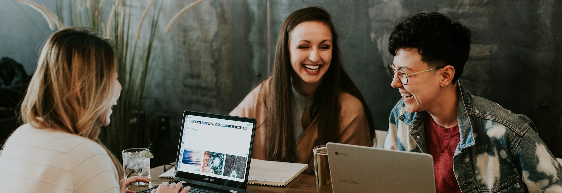 Three students sitting at a table with their laptops, talking and smiling