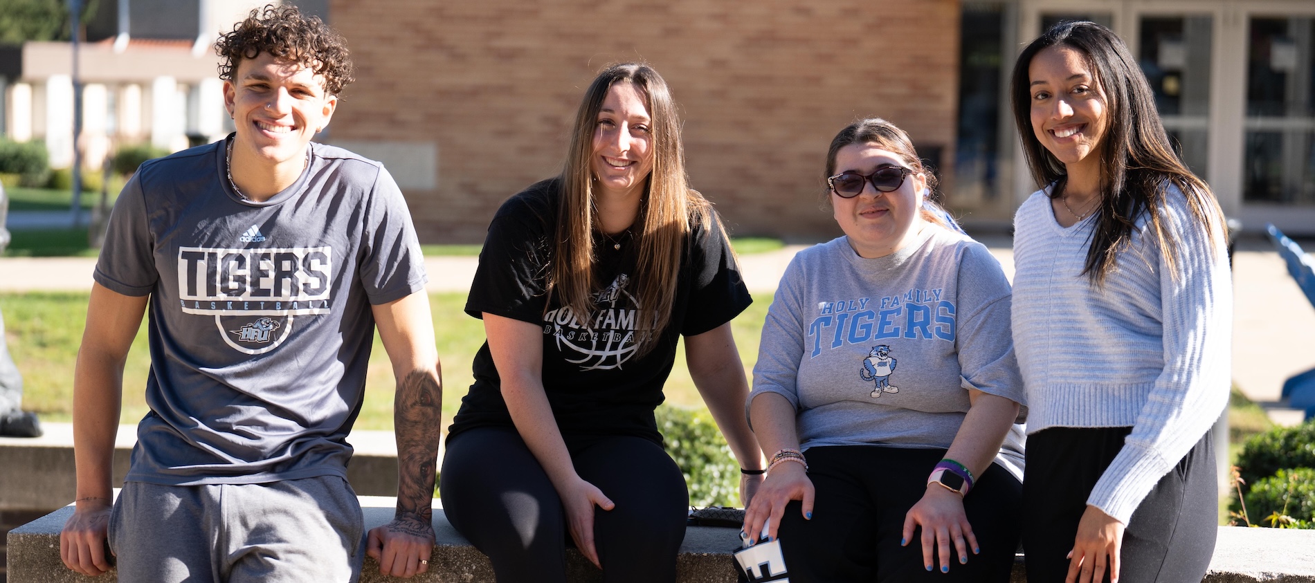 Four students standing and smiling outside on campus in front of the Library