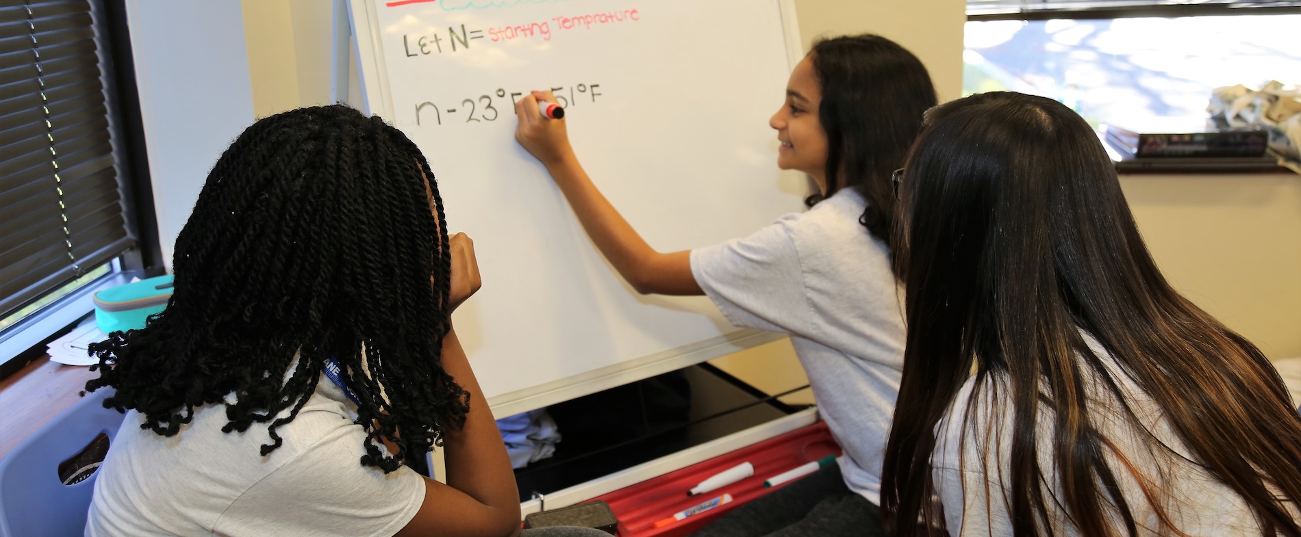 Three students solving equations on a whiteboard