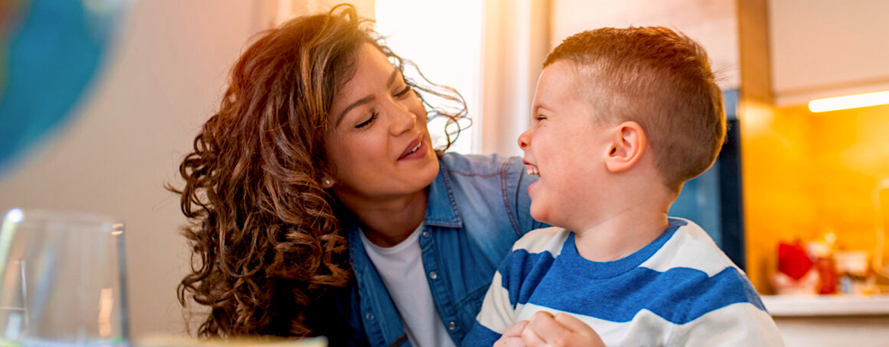 A child smiling and looking up at a caregiver in a sunny room