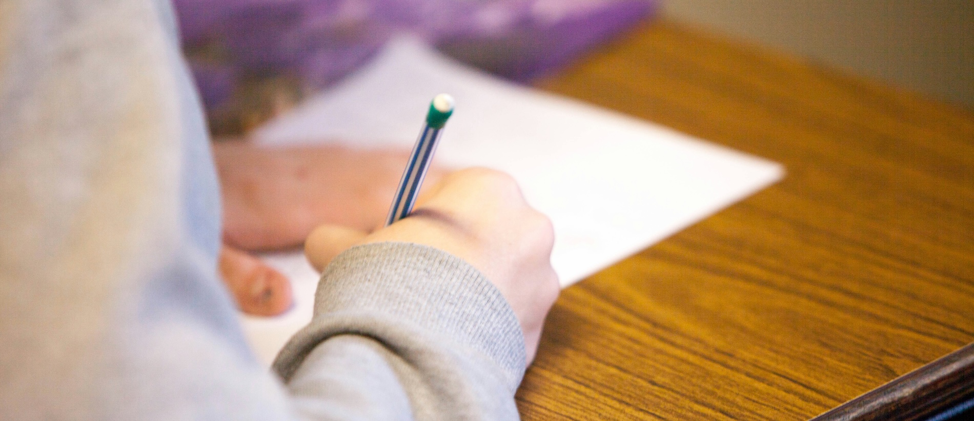 A desk with a test paper on it and a student's hand filling out answers with a pen