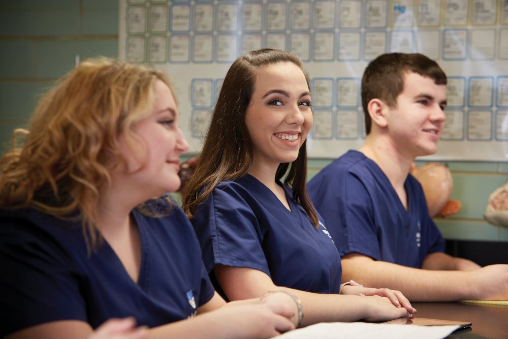 Three nursing students in scrubs smiling in the classroom