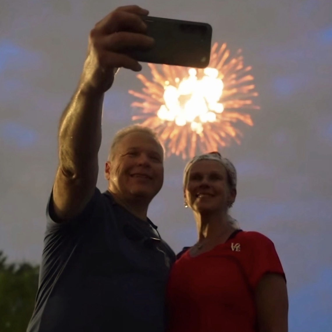 Two people taking a selfie with fireworks in the background