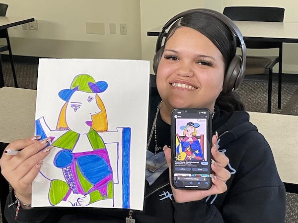 Student holding both her artwork and her phone displaying the artwork that inspired her