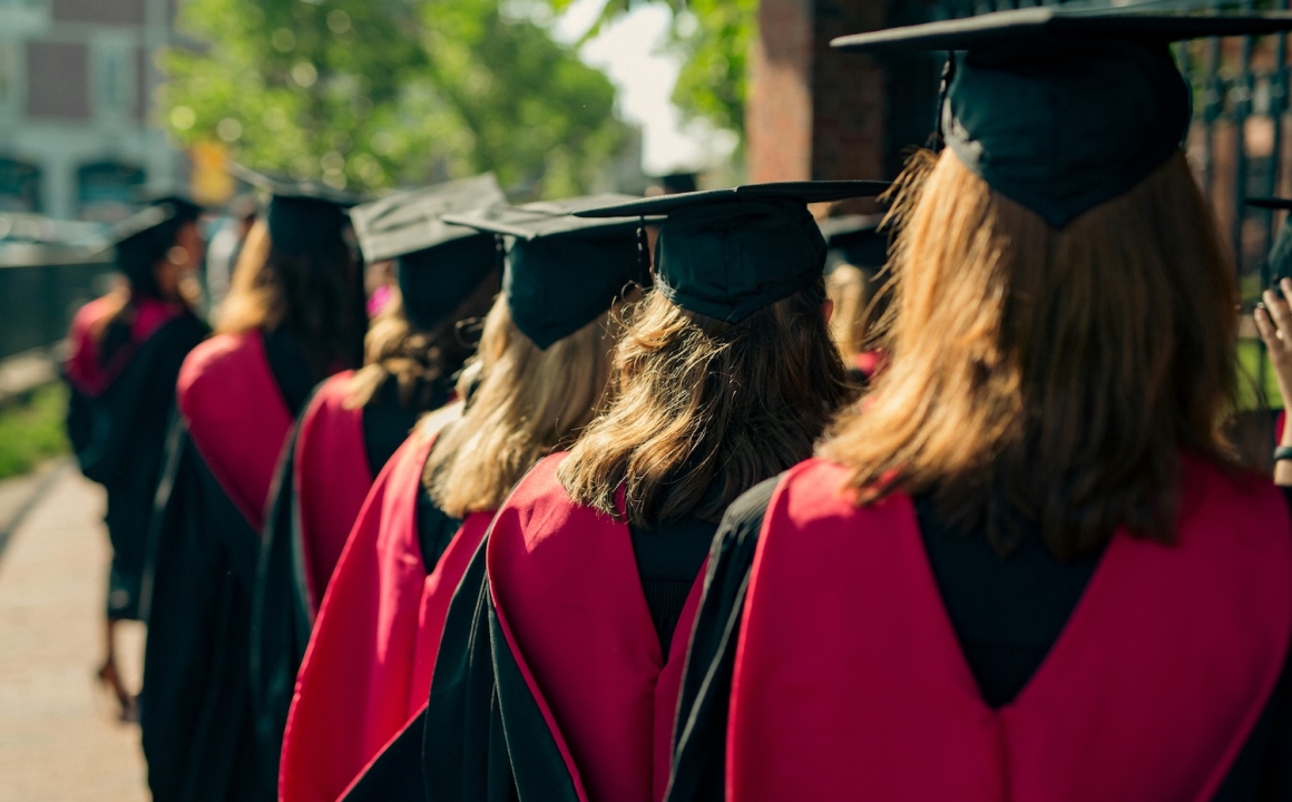 A group of college students in caps and gowns facing away from the camera