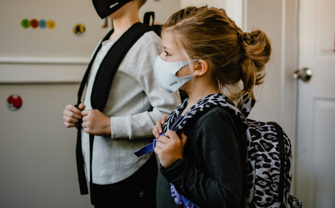 Two children wearing Covid masks and school backpacks