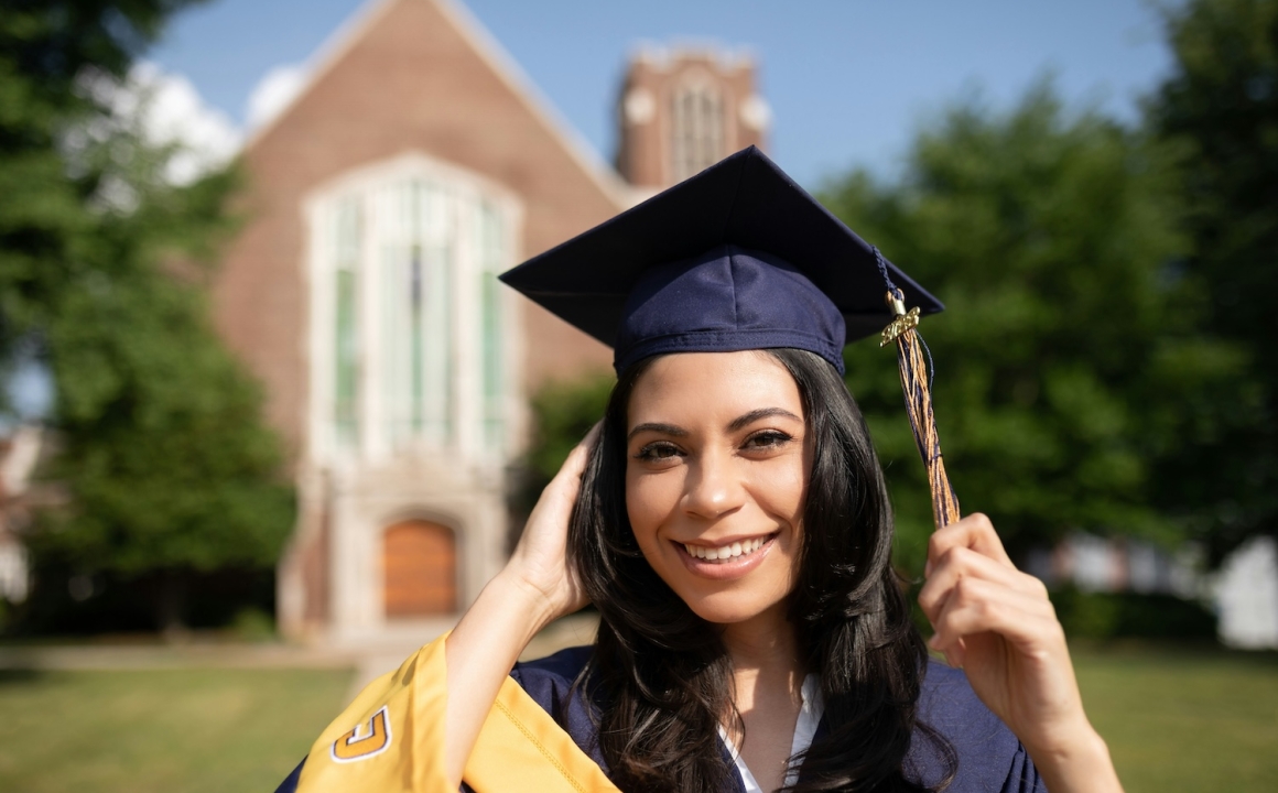 A female student on a college campus in a cap and gown smiling