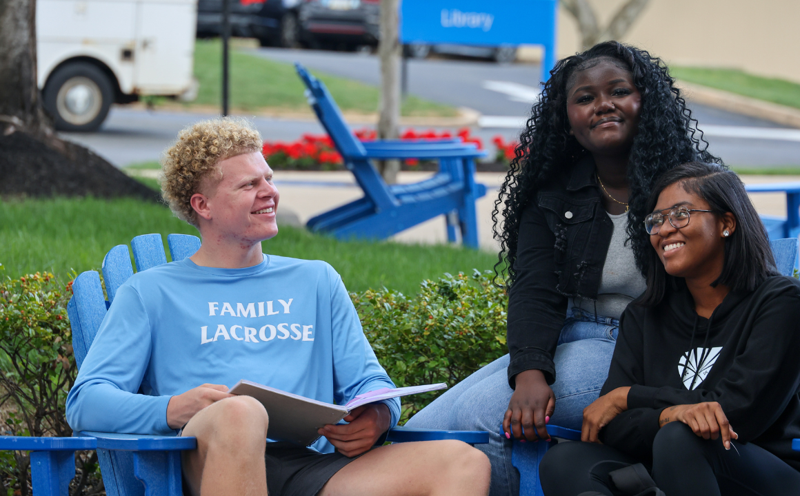 Three students sitting outside on campus talking and smiling
