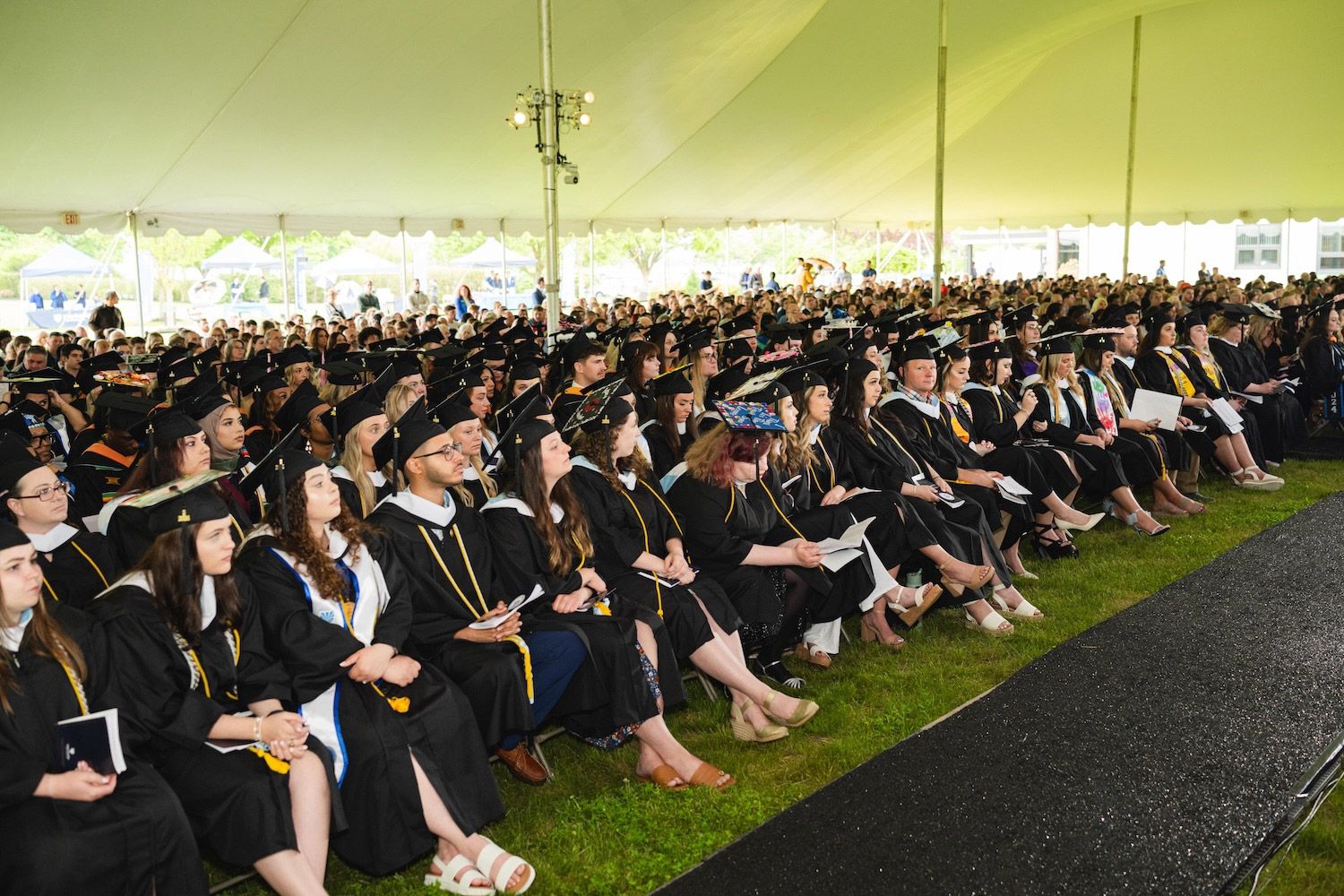 Large crowd of HFU students in caps and gowns sitting under a text during 2024's Commencement