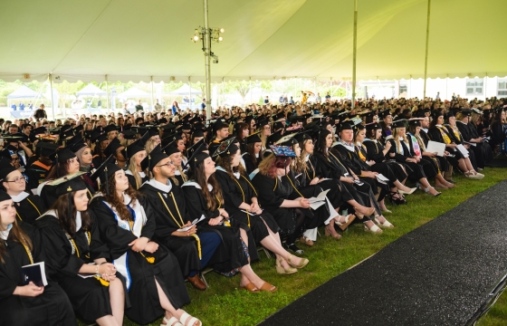 Large crowd of HFU students in caps and gowns sitting under a text during 2024's Commencement