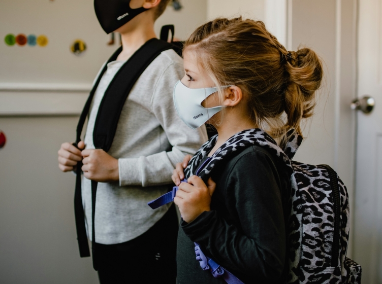 Two children wearing Covid masks and school backpacks