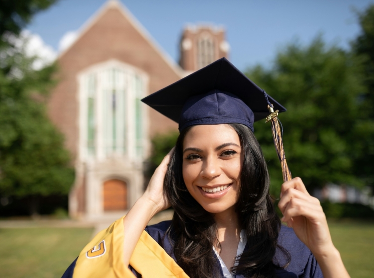 A female student on a college campus in a cap and gown smiling