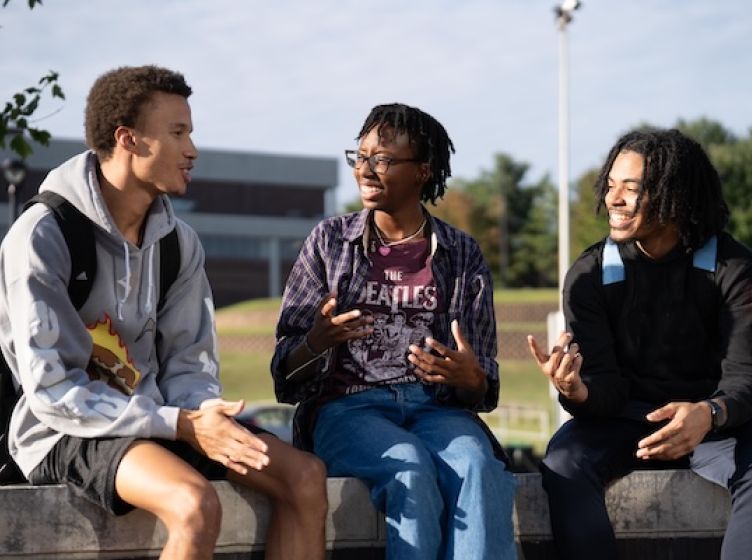 Three students sitting outside on campus talking and smiling